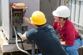 Two AC technicians repairing an industrial air conditioning compressor.
